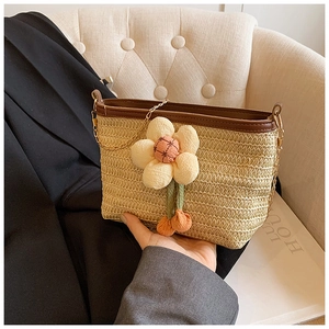 Détail du sac seau en paille tressée avec bordure cuir, chaîne et pendentif fleur