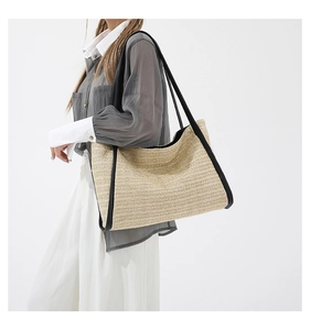 Detailed texture of hand-woven straw tote with premium black leather trim and long straps