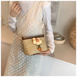 Détail du sac seau en paille tressée avec breloque fleurie et bandoulière dorée