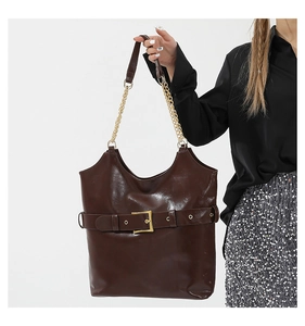 Détail d'un cabas marron foncé brillant avec boucle dorée vintage et bandoulière chaîne