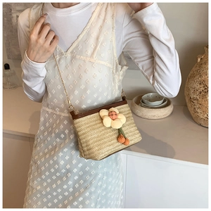Détail du sac seau en paille tressée avec breloque fleurie et bandoulière chaîne