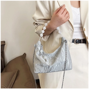 Close-up of metallic silver hobo bag with white beaded handle and elegant metal chain strap