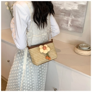 Détail du sac seau en paille tissée avec grande fleur crème et bandoulière chaîne dorée