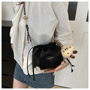 Detail of black drawstring bucket bag with gold metal corners and plush toy charm