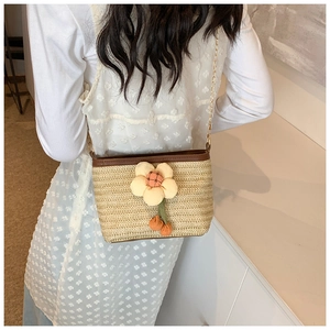 Détail d'un sac seau en paille tissée avec breloque fleurie et bandoulière chaîne dorée