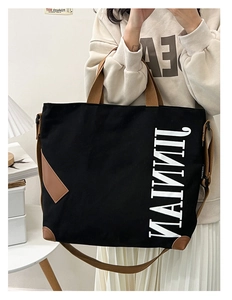 Détail du cabas en toile noire avec empiècements en cuir marron et logo JINNIAN blanc