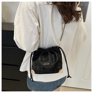 Detail of black drawstring bucket bag with gold metal corners and chain strap