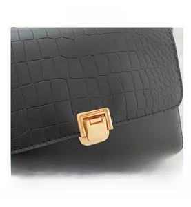 Detail view of black handbag featuring crocodile texture flap and golden metal clasp