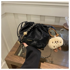 Detail view of black drawstring bucket bag with gold chain strap and plush charm
