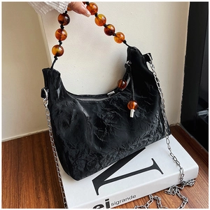 Close-up of black pleated PU bag with amber resin beads and fine silver chain detail