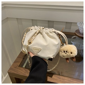 Detail of cream drawstring bucket bag with golden chain strap and plush animal charm