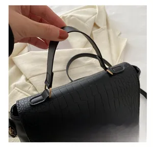 Close-up of black crocodile texture handbag featuring a golden metal lock and soft handle