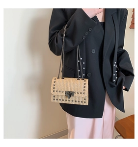 Détail du sac à bandoulière en paille tressée avec clous métalliques et fermoir rotatif