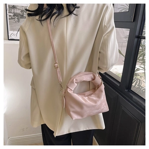 Pink pleated crossbody bag with a knot handle shown on a model in an elegant suit