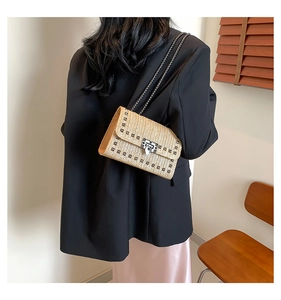 Détail d'un sac bandoulière en paille tressée avec clous et fermoir rotatif argenté