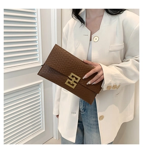 Close-up of brown quilted envelope clutch with golden geometric clasp held by a model