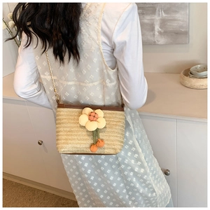 Détail du sac seau en paille tressée avec fleur 3D et bandoulière en chaîne dorée
