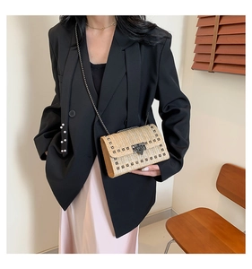 Détail du sac à bandoulière en paille tressée beige avec rivets métalliques et chaîne