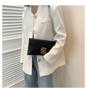 Close-up of black envelope clutch with crocodile texture and gold geometric metal clasp