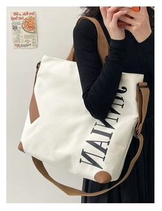 Détail du sac cabas en toile blanche avec garniture en cuir marron et texte latéral