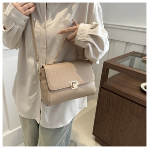 Detail of elegant crocodile-embossed flap and gold metal twist lock on beige crossbody bag