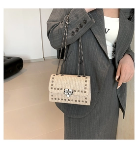 Détail du sac beige tressé à chaîne avec clous argentés porté sur un tailleur