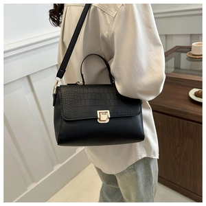Detail of black crocodile texture flap and gold buckle on a structured crossbody bag