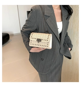 Détail d'un sac à rabat en paille tissée avec clous métalliques et bandoulière chaîne