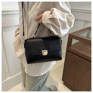 Detail of black crossbody bag with crocodile pattern flap and golden twist lock closure