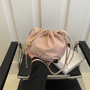 Pink drawstring bucket bag with gold chain strap and metal corners in lifestyle setting