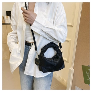 Detail of black pleated handle handbag with gold hardware and fashion tag in model context