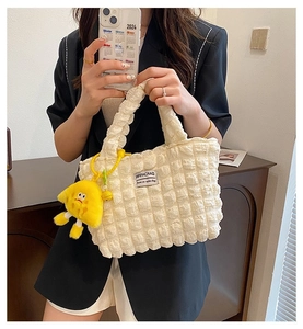 Detail of beige quilted tote with puffy bubble texture and yellow cartoon charm