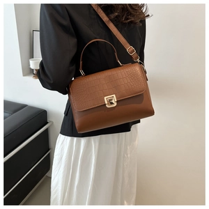 Detail of brown faux crocodile skin texture and gold metal twist lock on lady's handbag