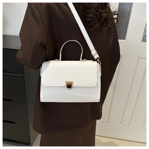 Detail of white crocodile texture flap and golden lock on a chic crossbody handbag