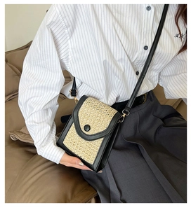 Detail of woven straw crossbody bag with black leather trim and golden metal hooks
