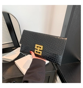 Detail of black crocodile texture envelope clutch bag with gold geometric metal clasp