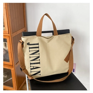 Gros plan sur un sac cabas en toile beige avec logo JINNIAN et sangle marron