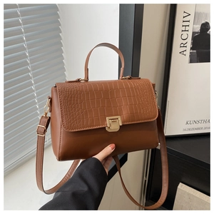 Detail of crocodile-textured leather flap and golden metal clasp on brown tote bag