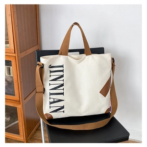 Gros plan d'un sac cabas en toile avec logo JINNIAN et coins de base en cuir marron