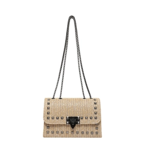 Sac bandoulière en paille avec clous noirs et bandoulière chaîne sur fond blanc