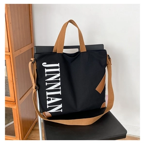 Détail du sac cabas en toile noire avec finitions en cuir marron et texte JINNIAN