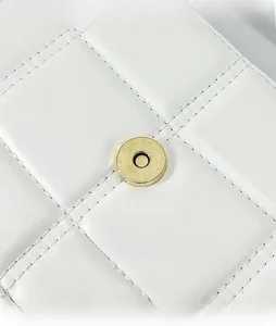 Close-up of golden magnetic snap button on white quilted leather bag with stitching