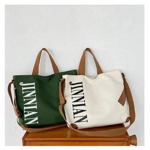 Détail des sacs fourre-tout en toile vert forêt et blanc avec logo JINNIAN et anses brunes