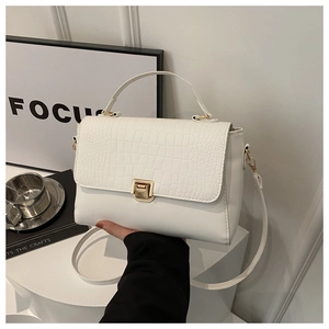 Detail shot of white crocodile texture bag with gold lock on minimalist white display stand