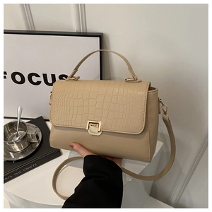 Detail of beige faux leather handbag with crocodile pattern texture and gold buckle