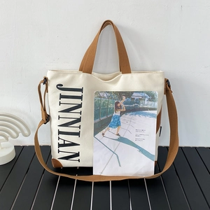Détail d'un sac cabas en toile avec sangles brunes, lettrage latéral et renforts d'angle