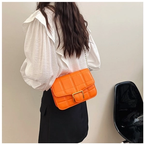 Close-up of an orange quilted crossbody bag with a gold square buckle on a model