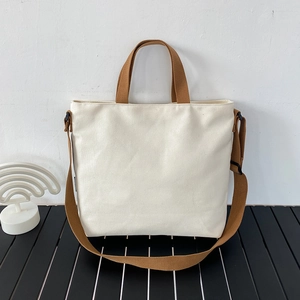 Détail du sac fourre-tout en toile crème avec anses brunes et bandoulière réglable