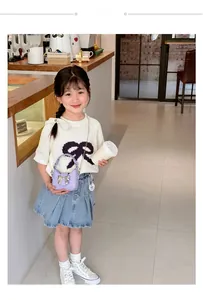 Girl in knit top and denim skirt carrying a purple mini purse with silver bow detail