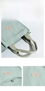 Detail of light green canvas tote bag showing magnetic buckle and leather logo patch